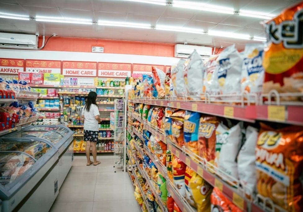 A woman browsing snack shelves at a supermarket, surrounded by various chips packages.