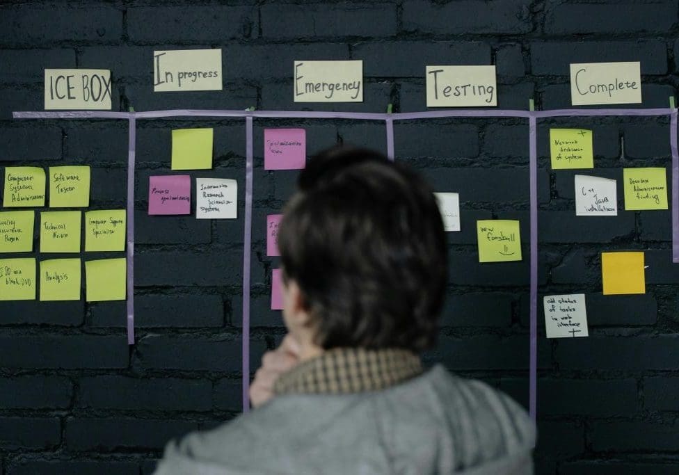 A man in an office reviews a scrum task board filled with sticky notes, planning strategy and organization.