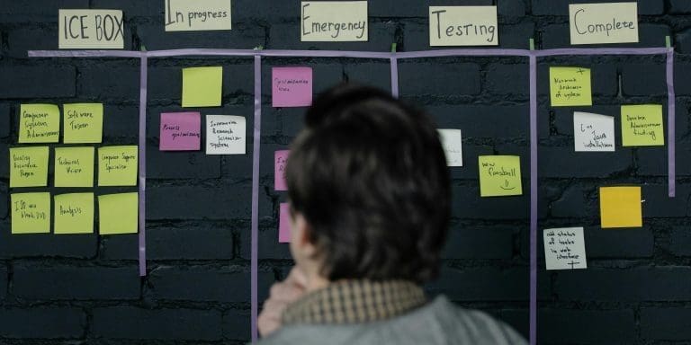 A man in an office reviews a scrum task board filled with sticky notes, planning strategy and organization.